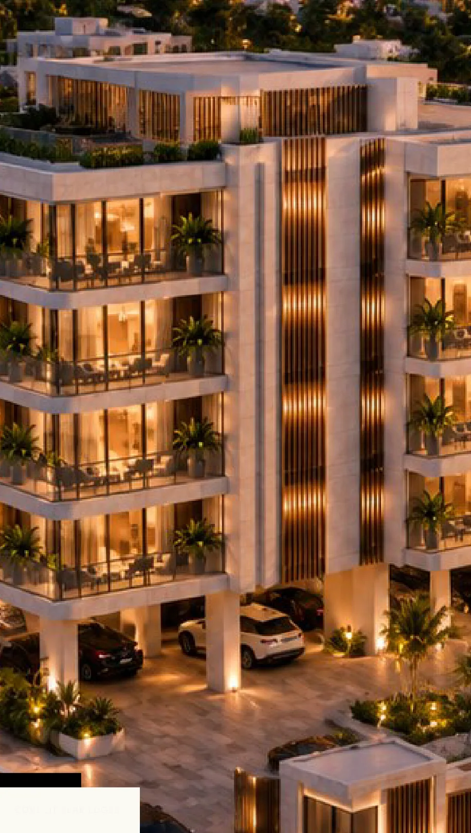 The building corner at dusk with the rooftop terrace visible above, bronze fin screens running the full height of the core, cove lighting picking out each curved slab edge, cars in the undercroft below.