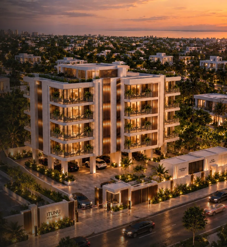 Elevated three-quarter view at sunset: the full building with four residential floors above an open, lit parking undercroft on piers, bronze fin screens to the stair core and flanks, curved balcony slabs with planting, gatehouse and 'ITUNU RESIDENCES' monument wall at the street, city and ocean horizon beyond.